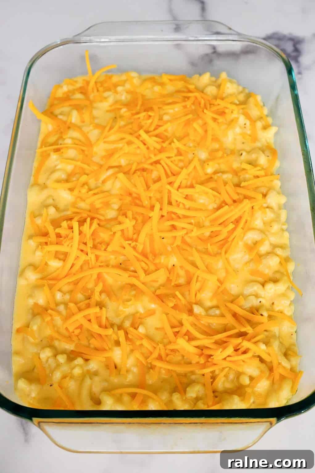 Old-Fashioned Baked Mac and Cheese with Ritz Cracker Topping 7 Unbaked old fashioned mac and cheese in a glass baking dish topped with shredded cheddar cheese, ready for the Ritz cracker topping.