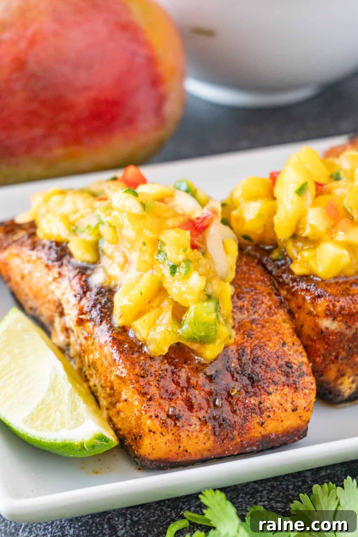 Grilled Salmon with Fresh Mango Salsa Recipe 2 Salmon topped with Mango Salsa on a white plate, with lime wedges near the salmon.
