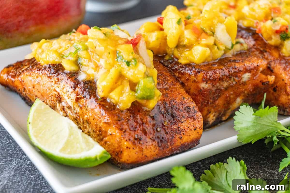 Grilled Salmon with Fresh Mango Salsa Recipe 11 salmon filets on a white plate with lime wedge and topped with mango salsa.