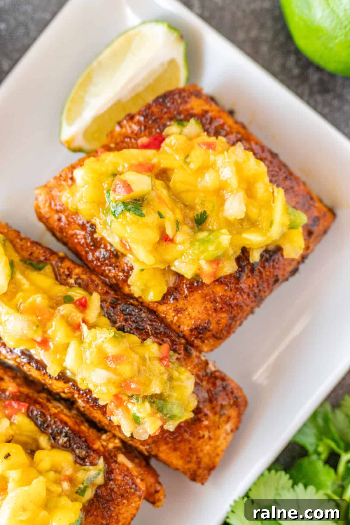 Grilled Salmon with Fresh Mango Salsa Recipe 13 Salmon topped with Mango Salsa on white plate, with lime wedges near salmon.