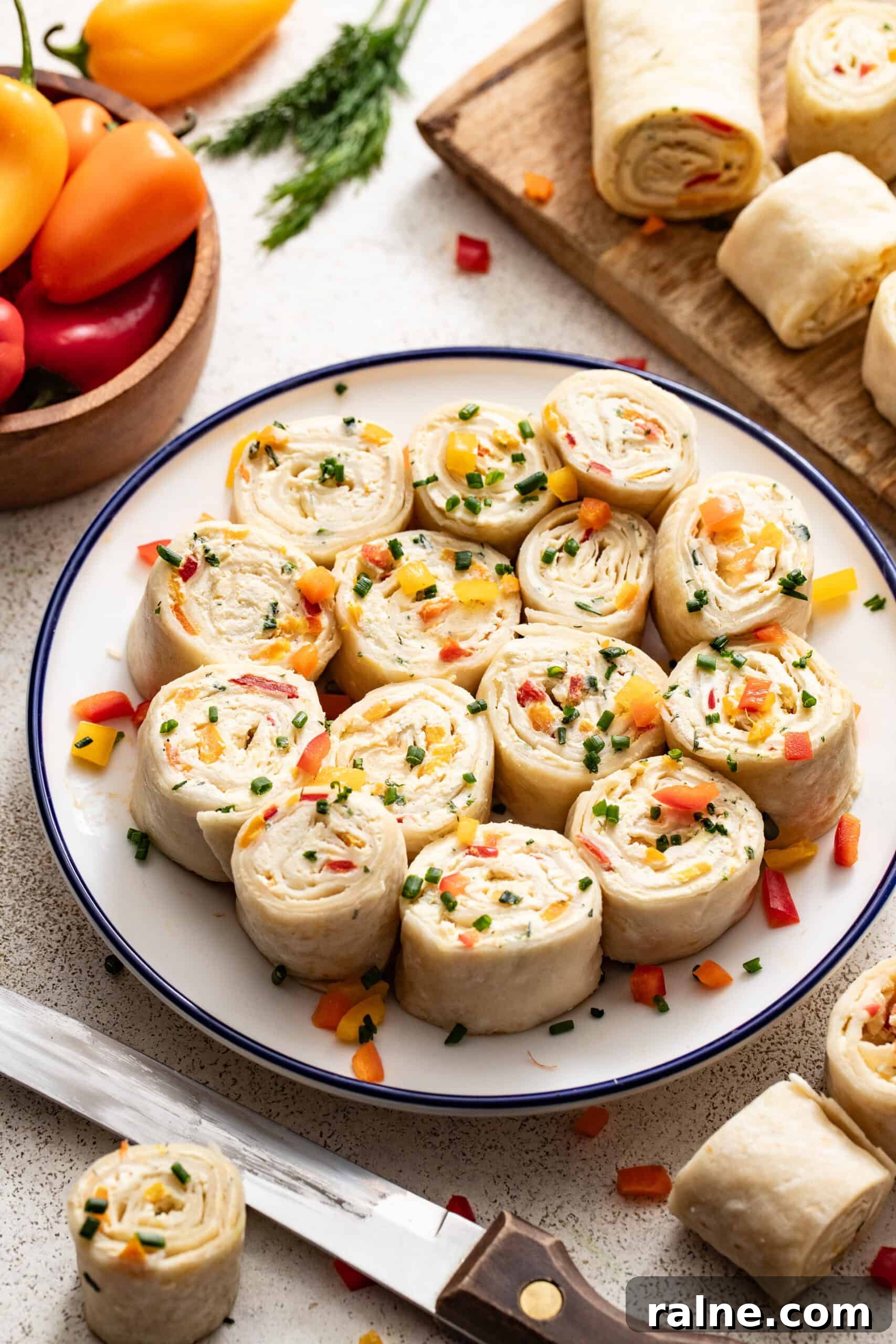 Cream Cheese Tortilla Roll-Ups: 5-Minute Party Appetizer Recipe 7 A plate of party pinwheels next to a cutting board with tortillas cut up and a knife.