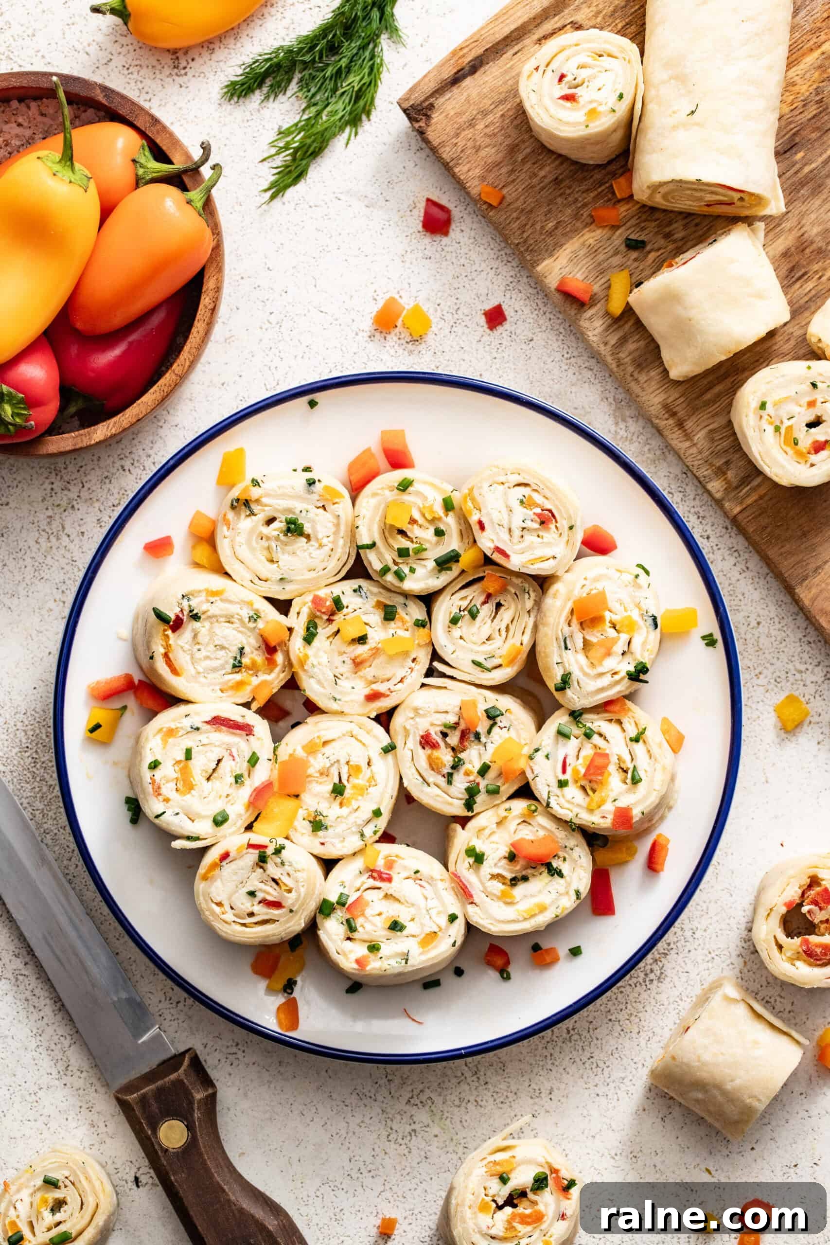 Cream Cheese Tortilla Roll-Ups: 5-Minute Party Appetizer Recipe 8 A plate of vegetable tortilla pinwheels with cream cheese and a bowl of peppers next to them.