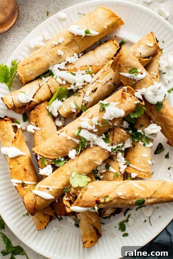 Cream Cheese Tortilla Roll-Ups: 5-Minute Party Appetizer Recipe 9 Crispy chicken taquitos on a white plate with sour cream dipping sauce, cilantro, and crumbled cheese.