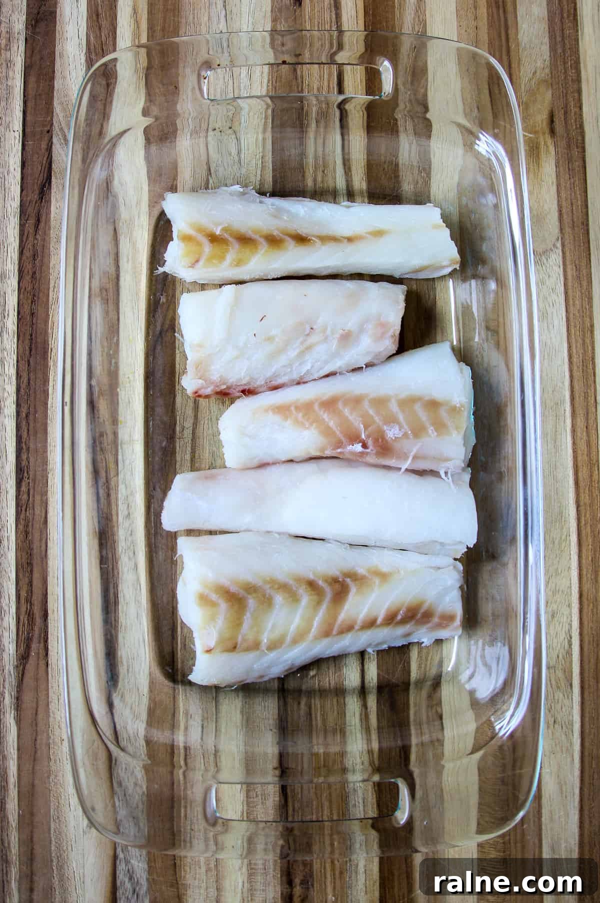 Cajun Blackened Cod Recipe — Crispy Spiced Pan-Seared Fish 4 Uncooked cod loins in a glass pan.