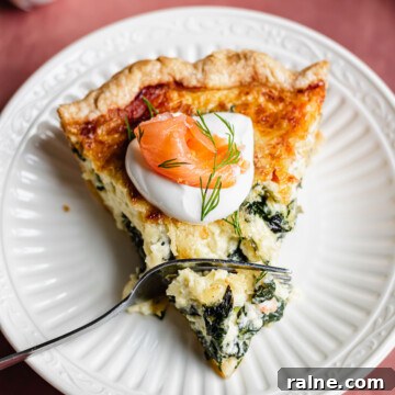 A slice of smoked salmon and spinach quiche on a plate with a fork in it.