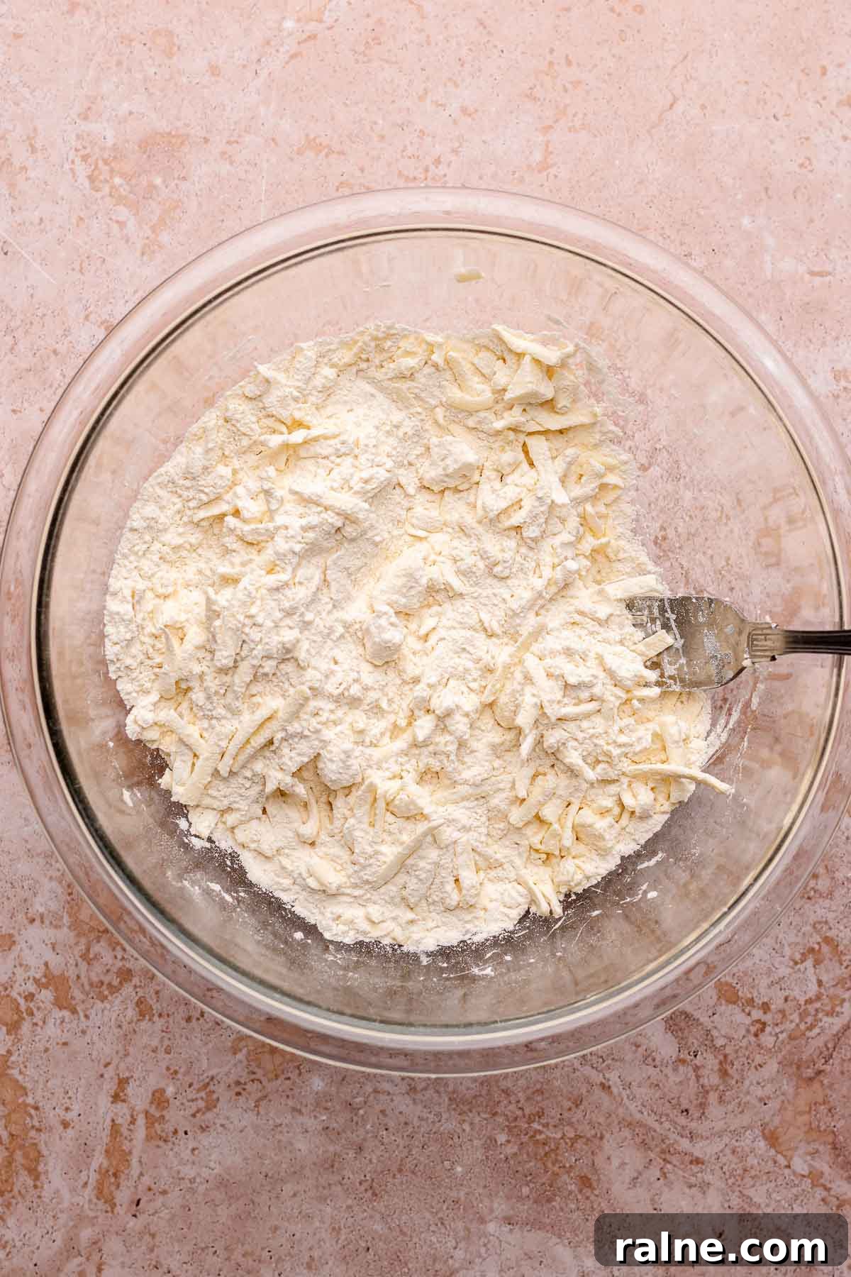 Savory Ham and Cheese Scones Recipe for Brunch or Snacks 5 A fork mixes dry ingredients and shredded butter in a bowl.