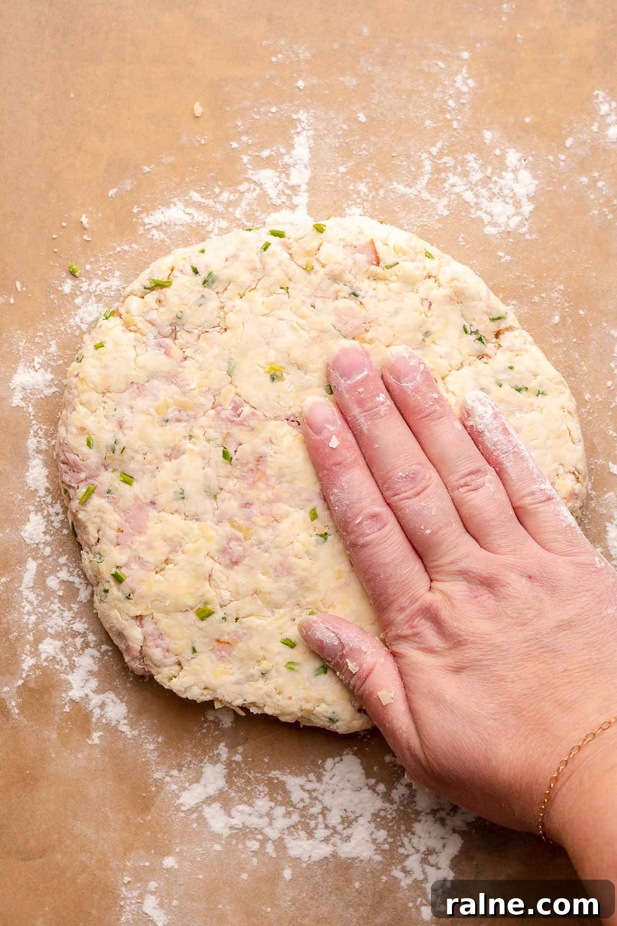 Savory Ham and Cheese Scones Recipe for Brunch or Snacks 8 A hand pats scone dough into a circle on a piece of parchment paper.
