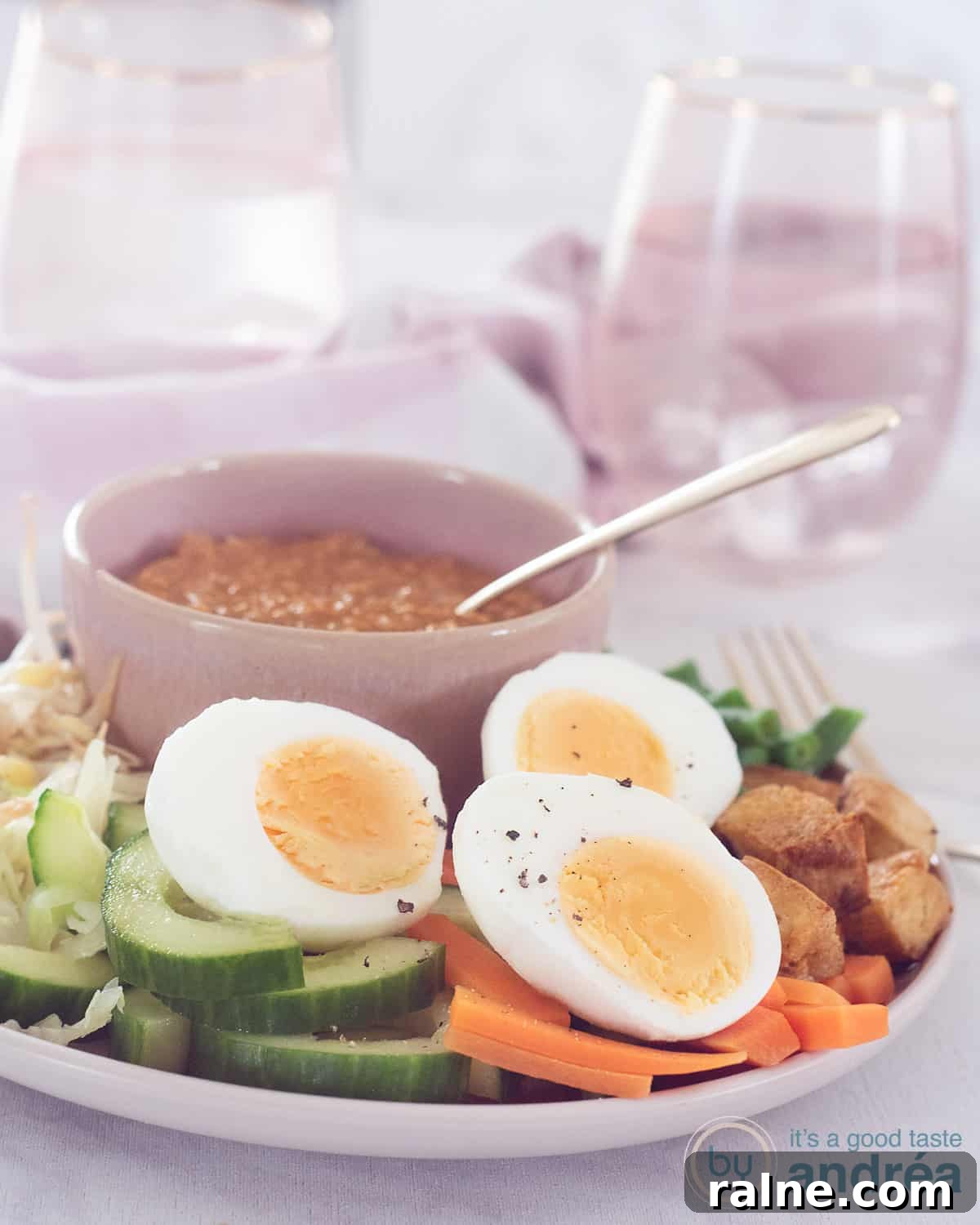 A pink plate with poached vegetables, eggs and tofu with a pink bowl of satay sauce.