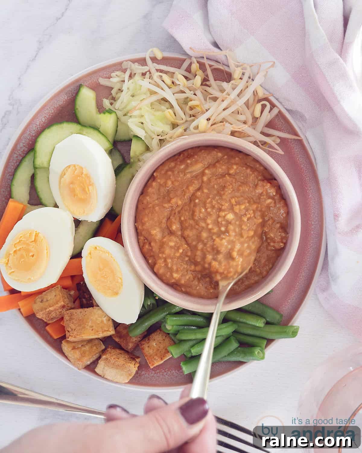 A photo from above of a pink plate with beans, tofu, carrots, cucumber and bean sprouts with eggs: gado gado with satay sauce