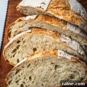 A loaf of no knead white bread sliced on a wooden board.