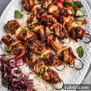 A platter with rice, chopped salad, sumac onions and harissa chicken skewers.