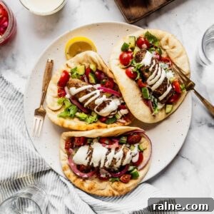 Plate with three turkey kofta wraps garnished with tahini sauce, pickled onions and chopped salad with cherry tomatoes and cucumbers.