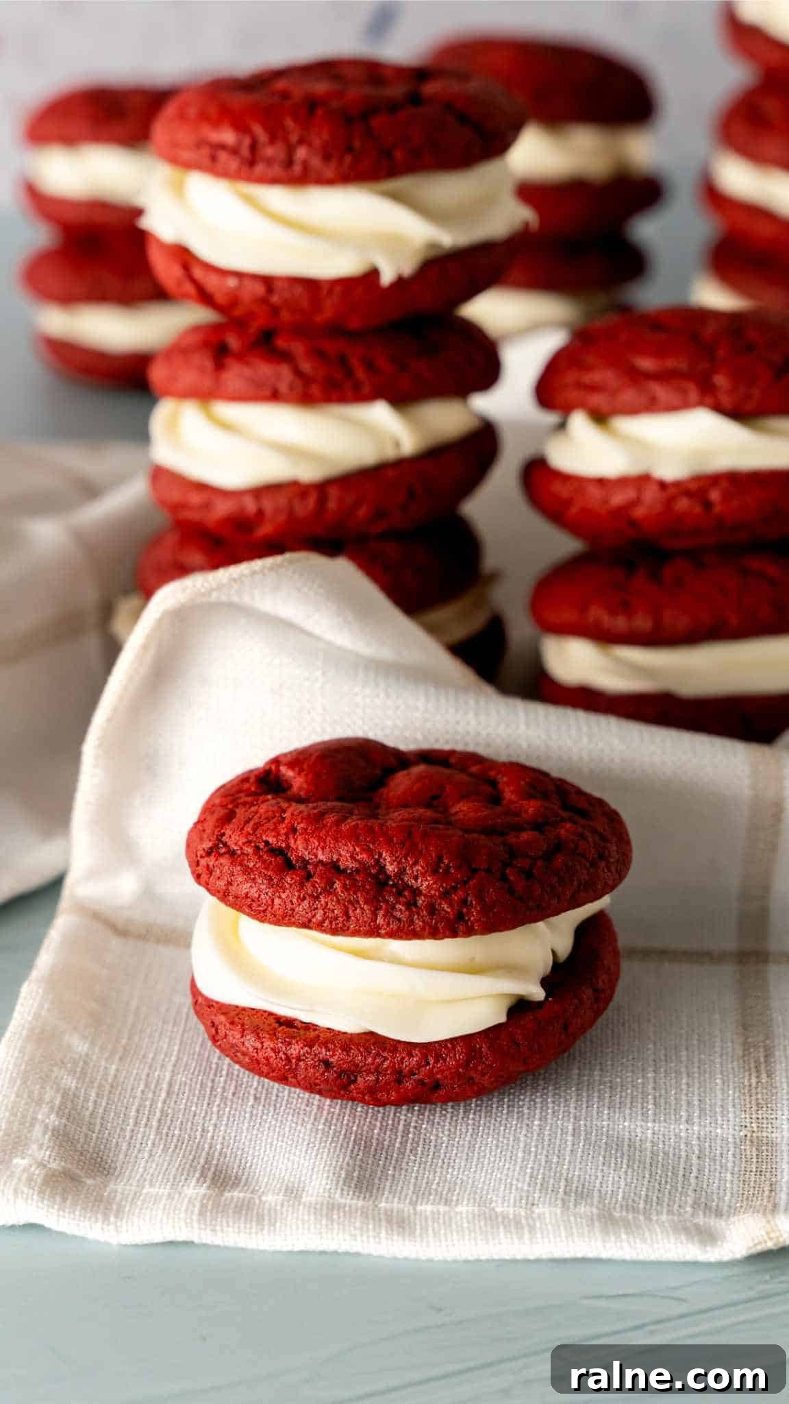Decadent Red Velvet Whoopie Pies Recipe for Perfect Sandwich Cookies 5 A red velvet whoopie pie with stacks of whoopie pies in the background.
