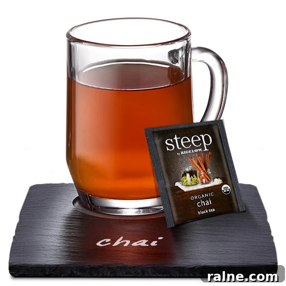 Glass mug of chai tea on a slate coaster labeled 'chai,' with a Steep by Bigelow Organic Chai tea bag beside it.