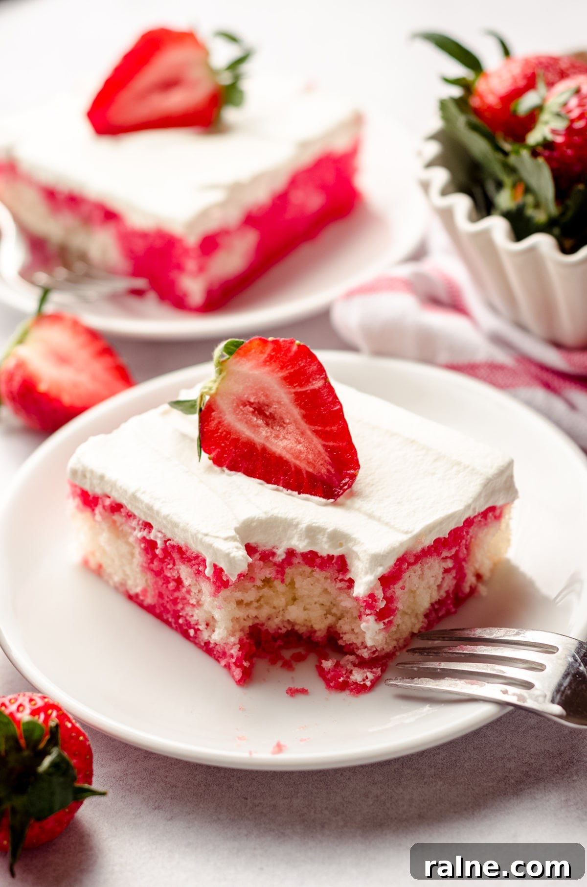 Strawberry Jello Poke Cake Recipe — Moist, Creamy Dessert 16 slice of strawberry poke cake on a plate with a bite taken out of it with a fork