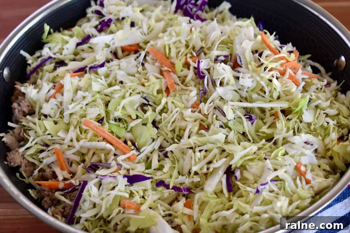 Coleslaw mix added to the skillet on top of the cooked meat. 