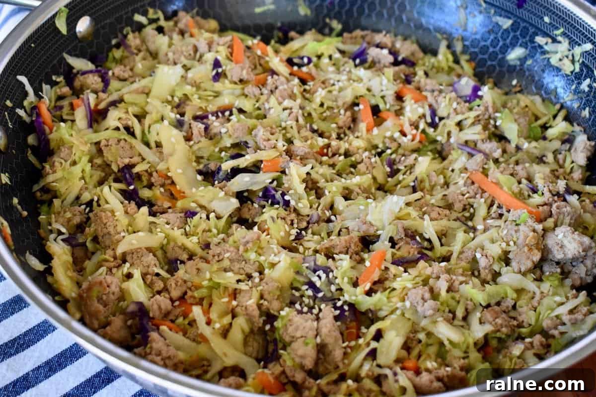 Egg roll in a bowl with ground turkey in a large skillet with sesame seeds sprinkled on top. 