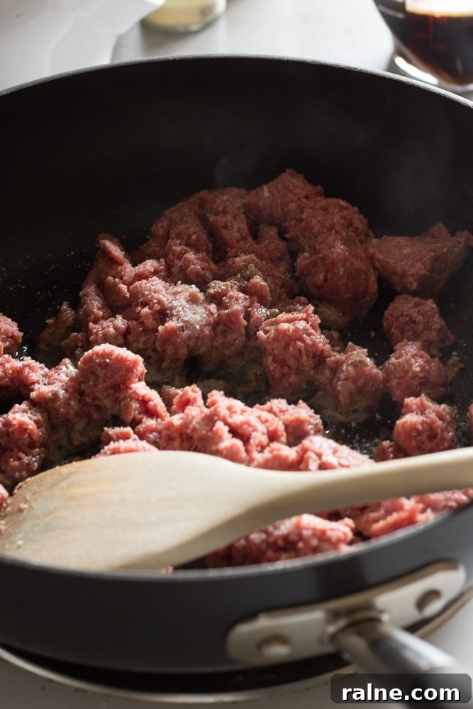 Ground beef cooking on a stovetop in a black pan with a wooden spoon.