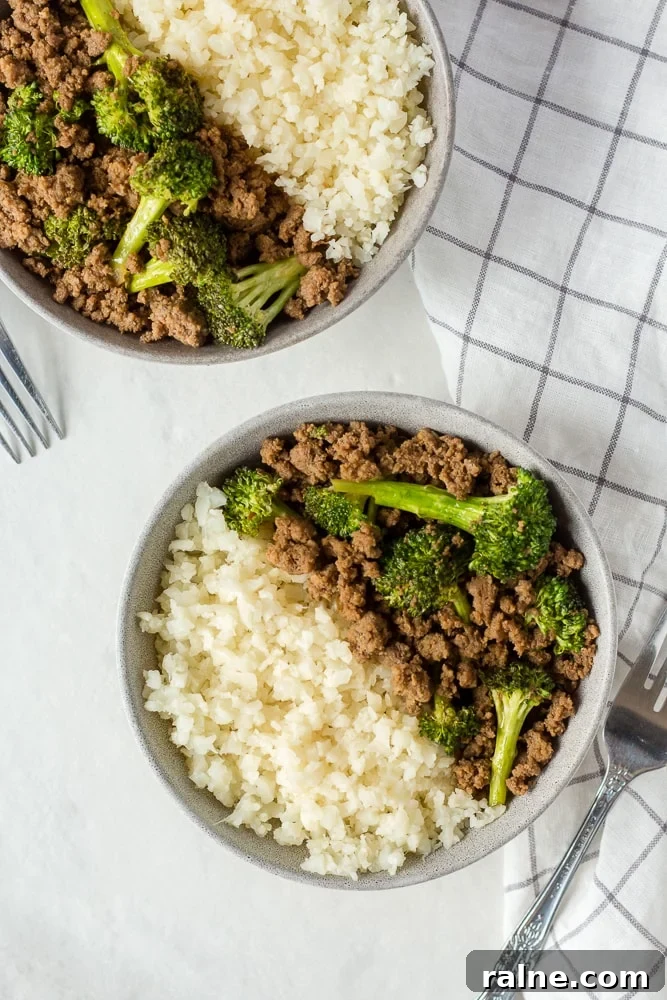 Top down shot of two gray bowls with ground beef, broccoli, and cauliflower rice on a white background.