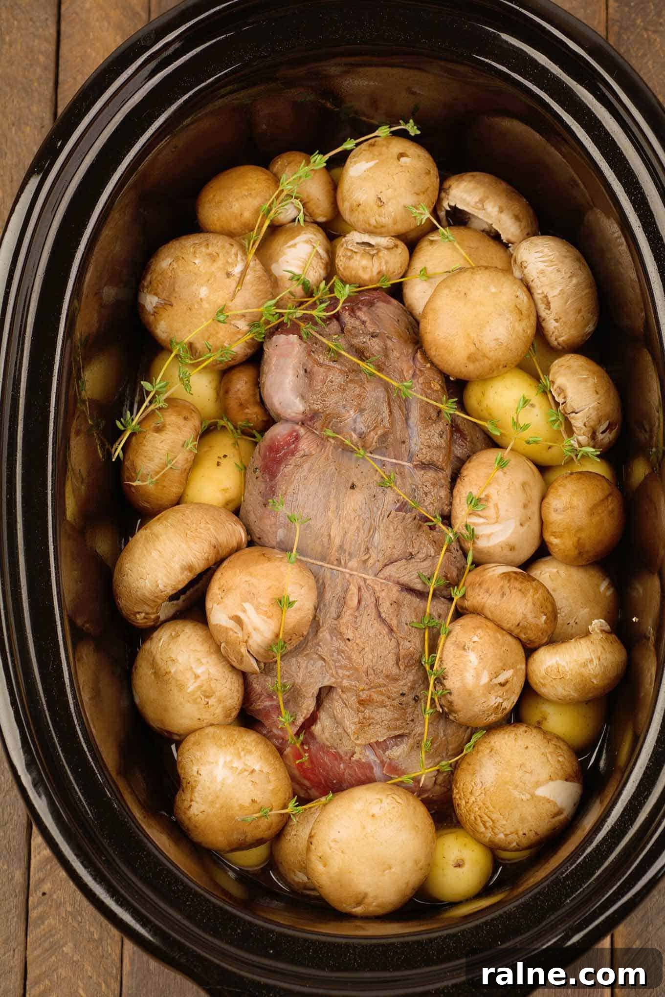 Slow Cooker Beef Pot Roast with Mushrooms and Red Wine香 3 Browned, uncooked, boneless chuck roast in the slow cooker surrounded by baby potatoes and mushrooms.