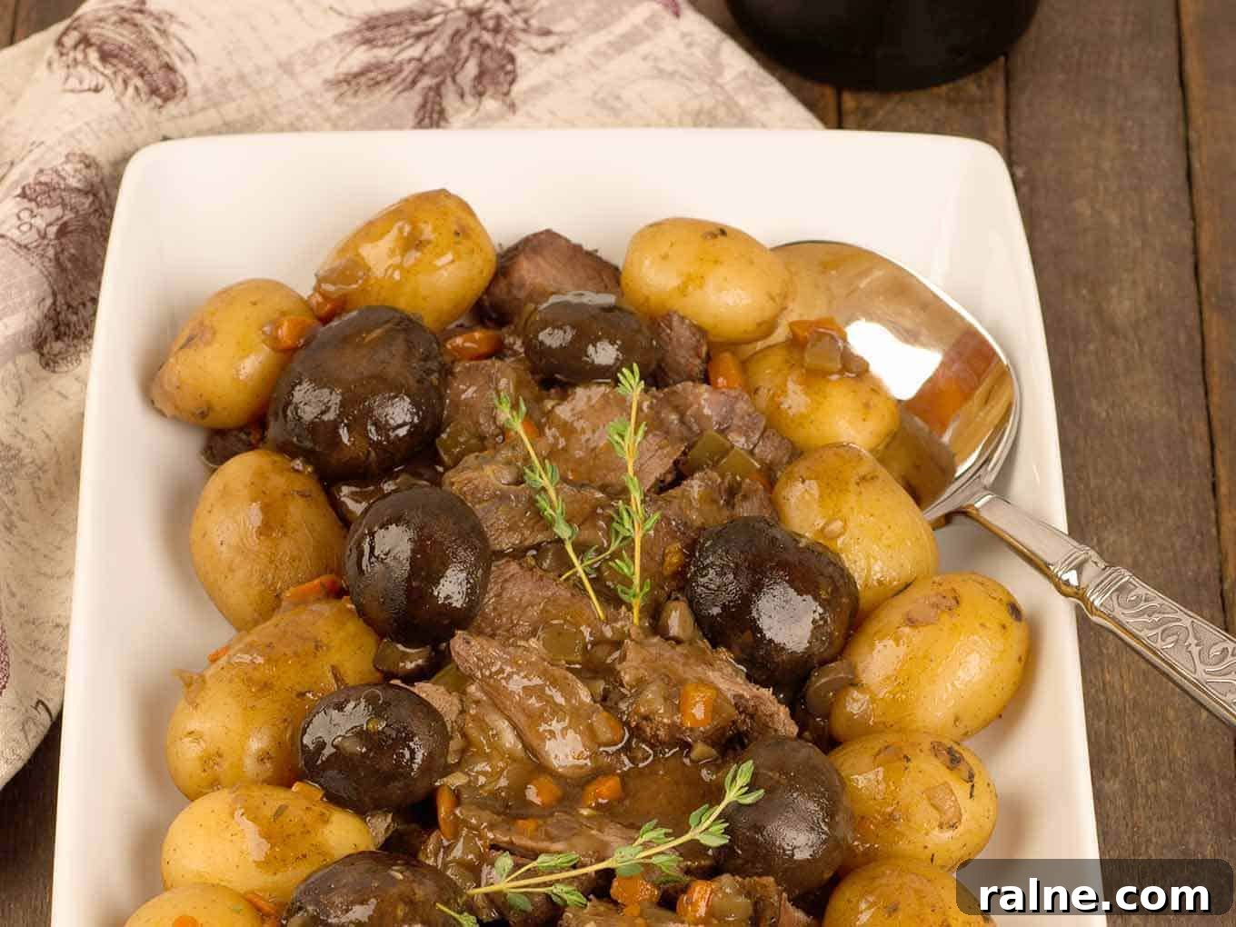 Slow Cooker Beef Pot Roast with Mushrooms and Red Wine香 4 A serving platter of sliced slow-cooker pot roast surrounded by braised mushroom caps and baby potatoes, garnished with a sprig of fresh thyme.