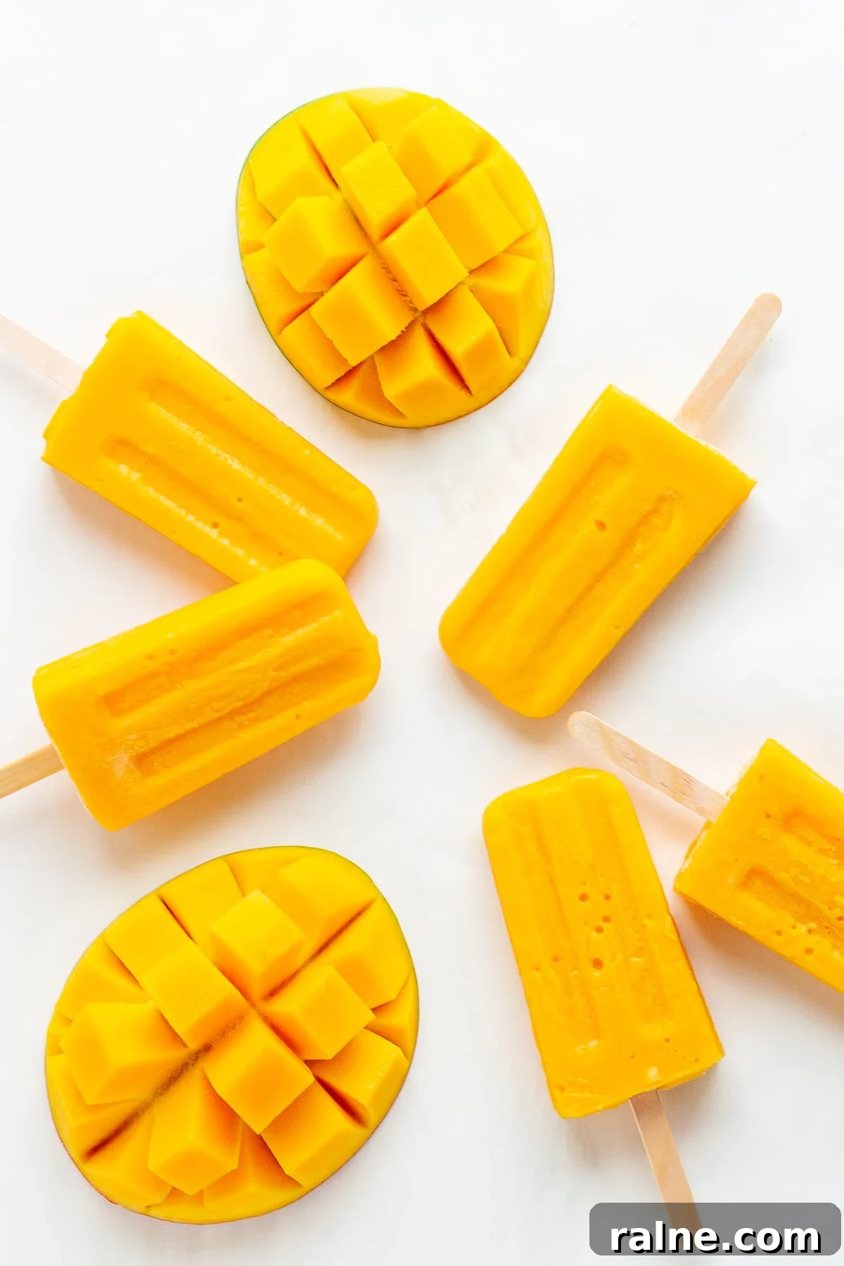 Mango popsicles and fresh mango halves on a white background.