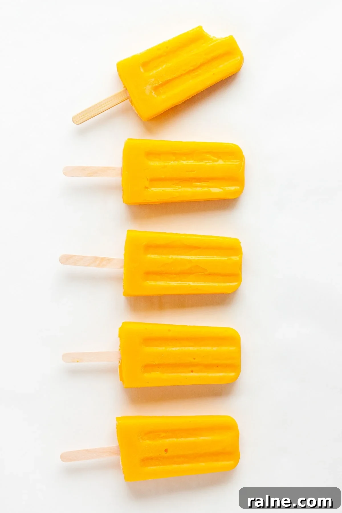 Vertical row of mango popsicles on a white background.