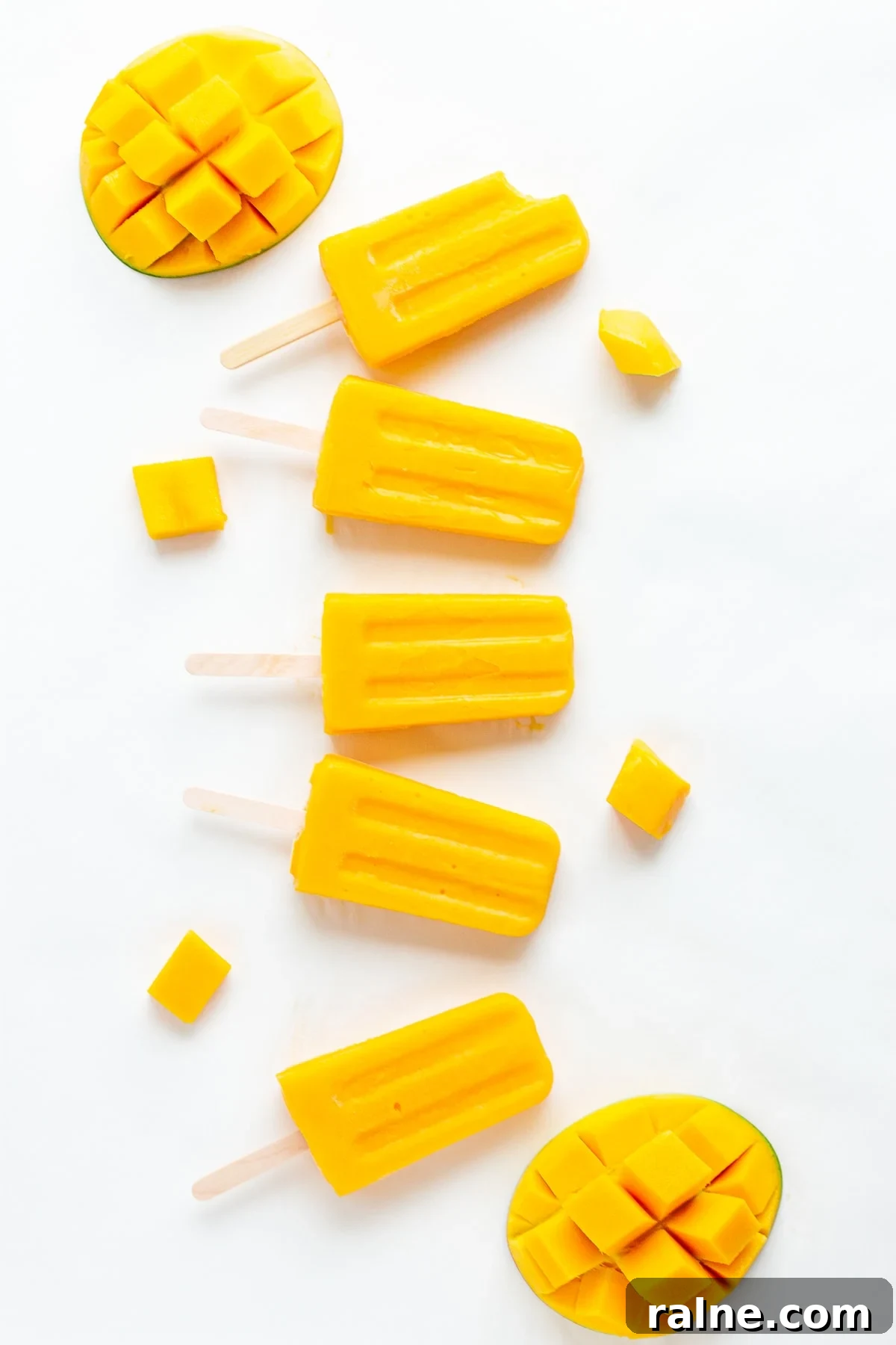 Mango popsicles and fresh mango displayed on a white background.