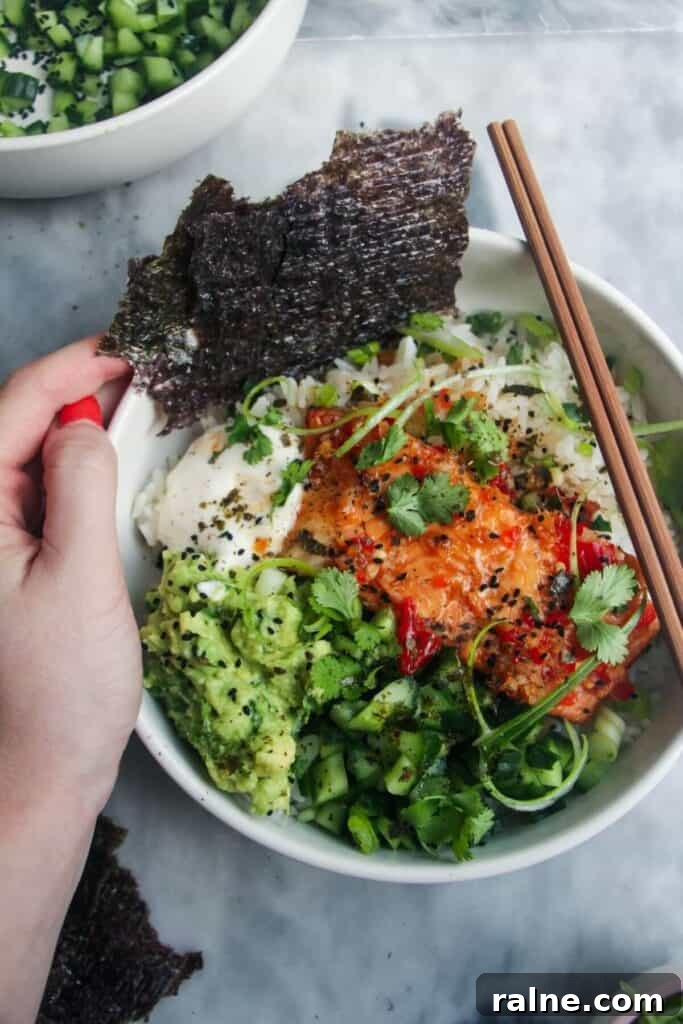 Spicy Tuna Crispy Rice Paper Cups Recipe for Impressing Guests 13 Hand holding a white bowl with salmon and colourful vegetables on rice.