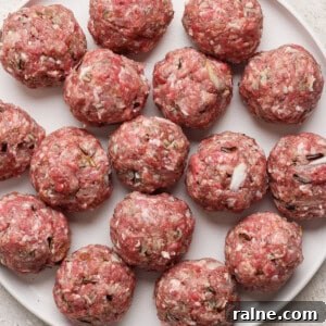 A plate filled with raw, evenly-sized meatballs, arranged in a circular pattern on a white surface.