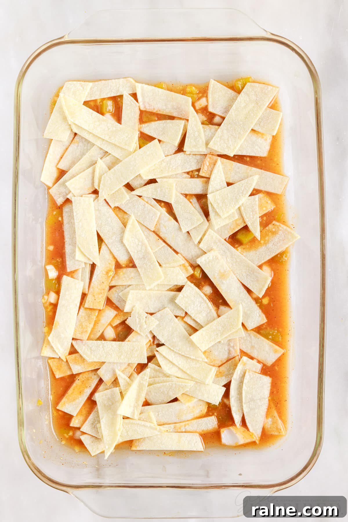 strips of corn tortillas placed on turkey enchilada casserole sauce mixture in a 9x13