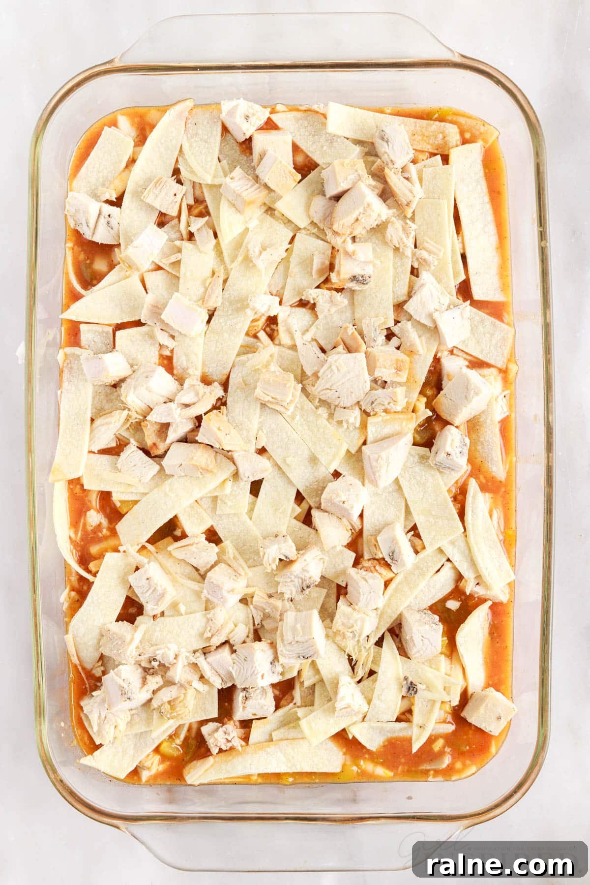 pieces of turkey layered on top of corn tortilla strips in glass 9x13