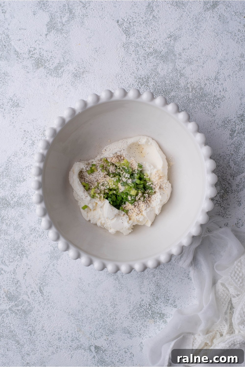 Crispy Cream Cheese Rangoon Wontons: Easy Homemade Recipe 5 A decorative white bowl filled with cream cheese, green onion, and spices.