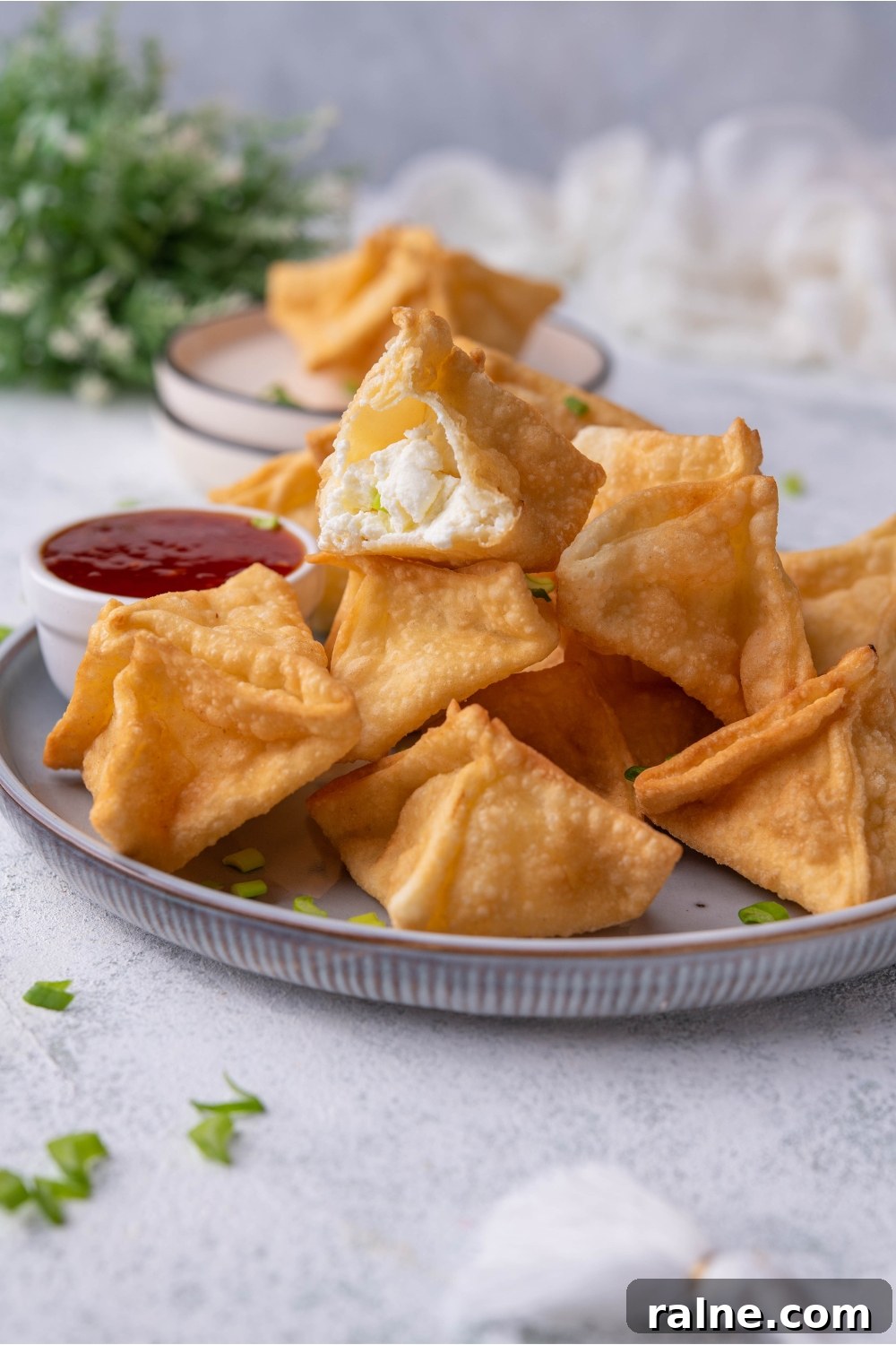 Crispy Cream Cheese Rangoon Wontons: Easy Homemade Recipe 10 A pile of Panda Express cream cheese rangoon piled high on a plate with a serving of dipping sauce. A bite has been taken out of one of the rangoon.
