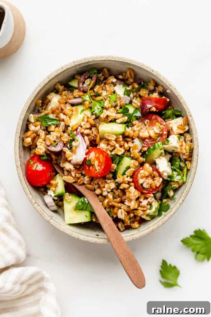 Mediterranean Farro Salad with Feta, Cucumber & Olives 2 a bowl of Greek farro salad with a wood spoon in it