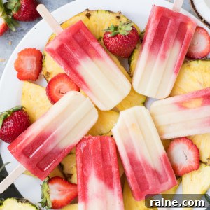 Miami Vice Mocktail Popsicles: Refreshing Raspberry Piña Colada Treats 5 A plate of pineapple slices topped with Miami Vice popsicles, surrounded by fresh strawberries and coconut pieces.