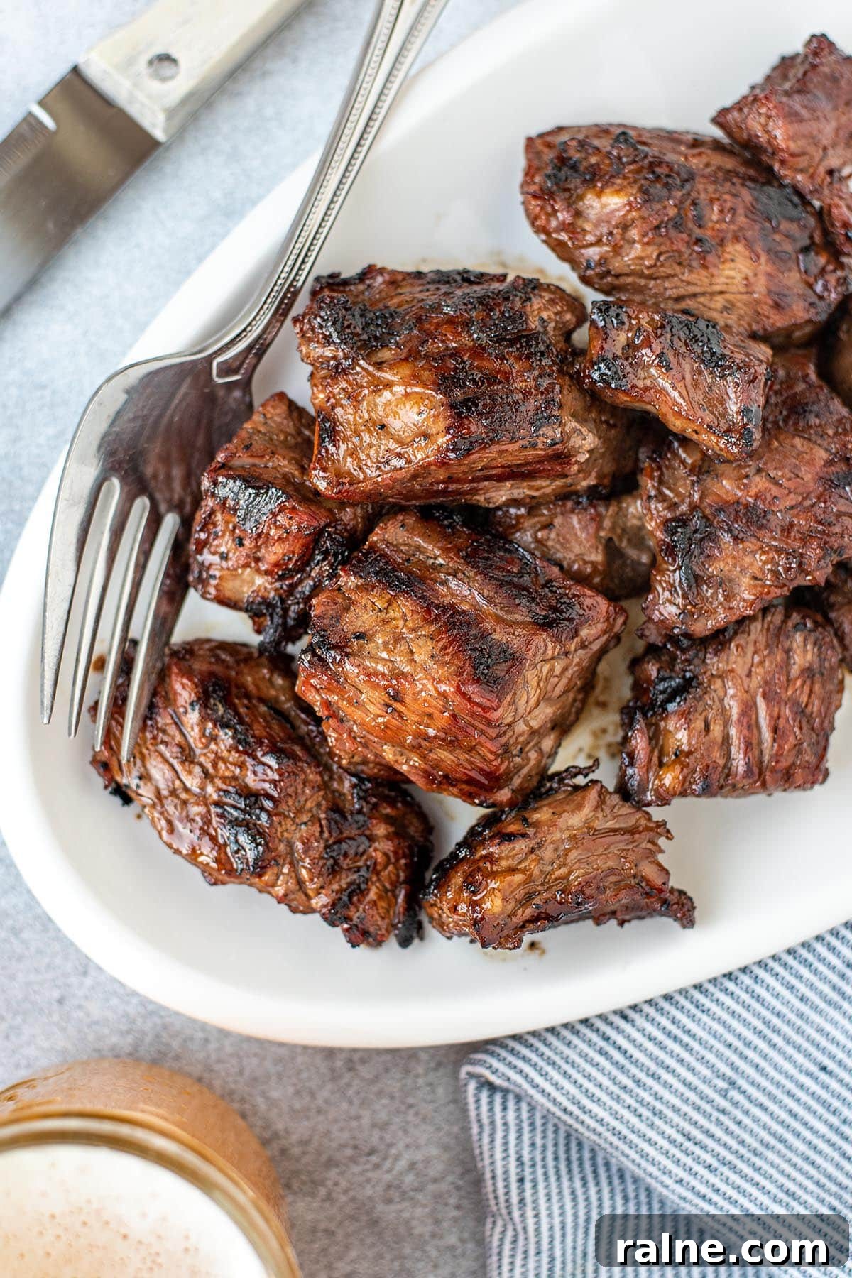 Beer Teriyaki Marinated Steak Tips Recipe 2 Perfectly caramelized steak tips on a white serving plate pictured with a fork and knife.