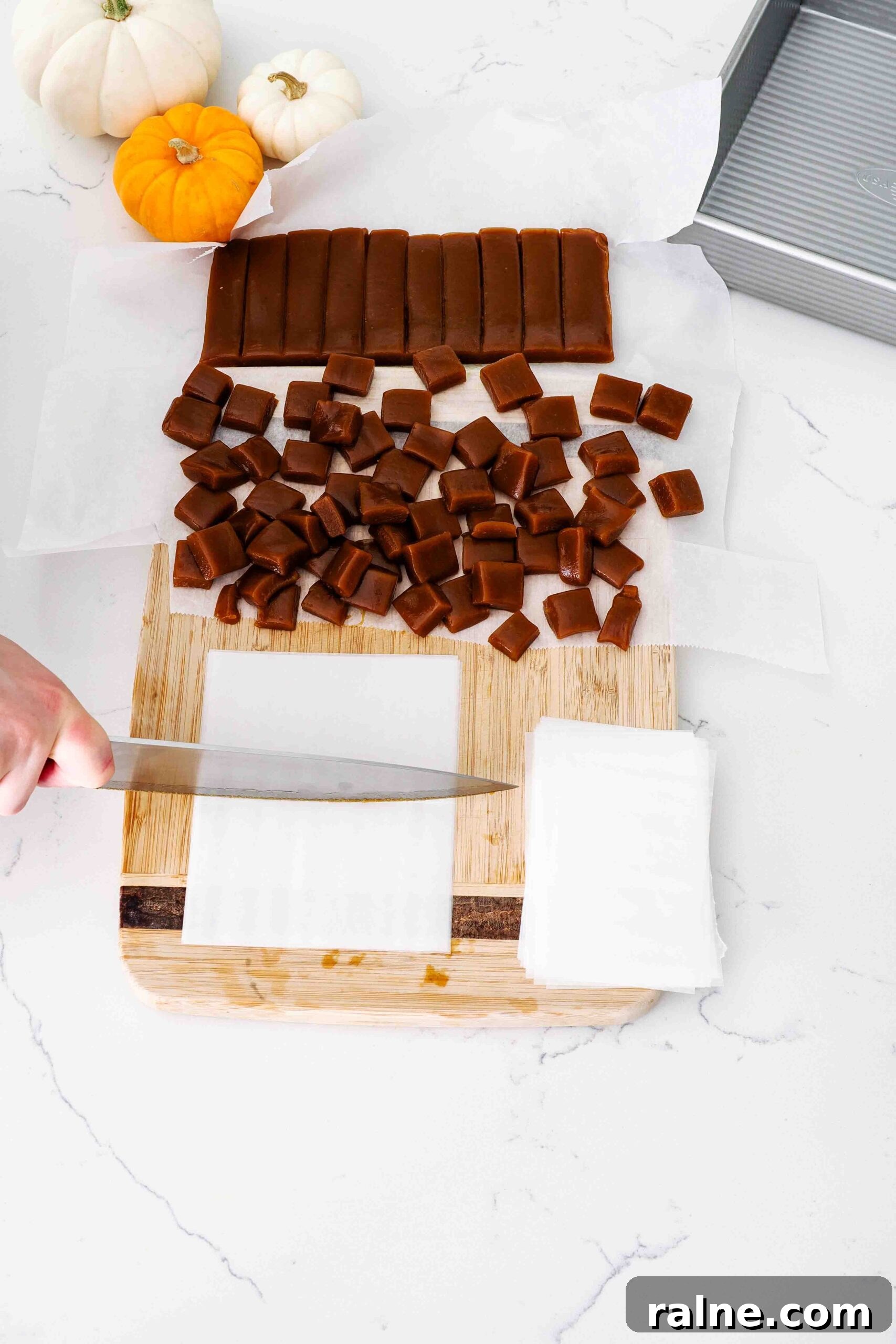 Pumpkin Spice Caramels Recipe: Homemade Fall Candy Guide 14 A knife cuts pre-cut wax paper pieces in half on a cutting board with caramels.