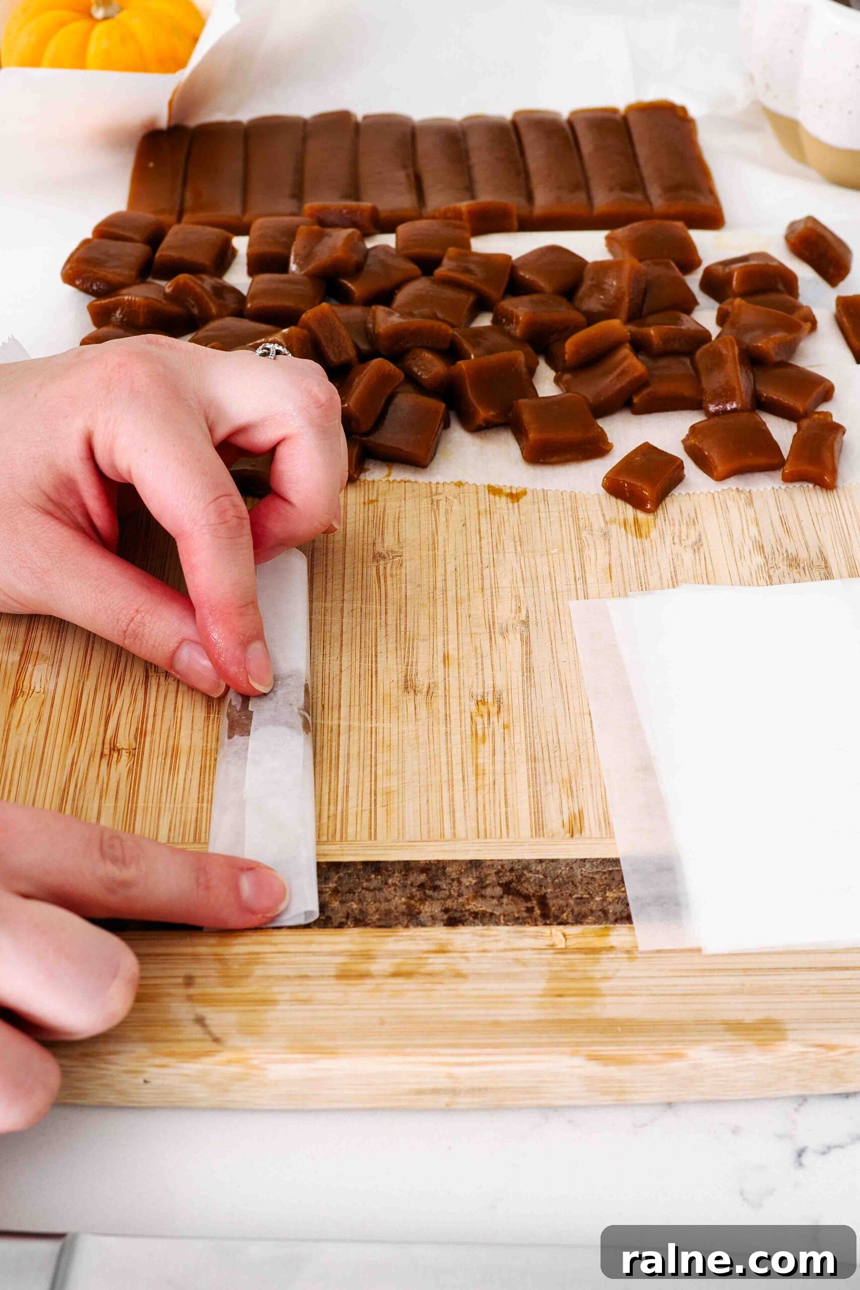 Pumpkin Spice Caramels Recipe: Homemade Fall Candy Guide 15 Two hands fold wax paper over a pumpkin spice caramel.