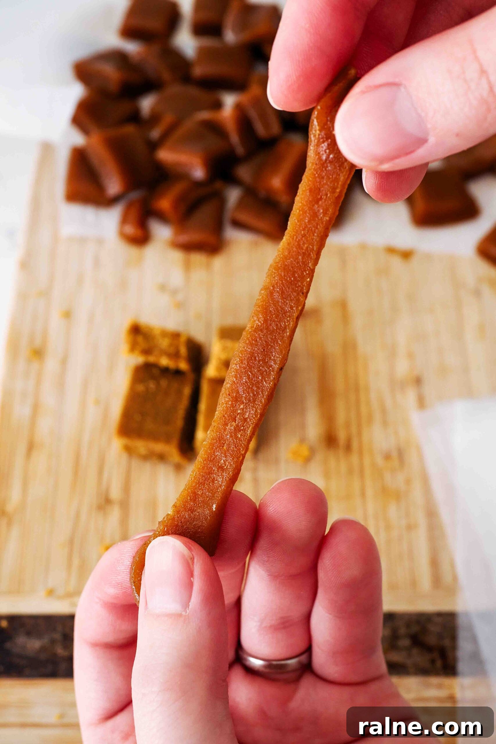 Pumpkin Spice Caramels Recipe: Homemade Fall Candy Guide 18 Two hands stretch a homemade pumpkin caramel a few inches.