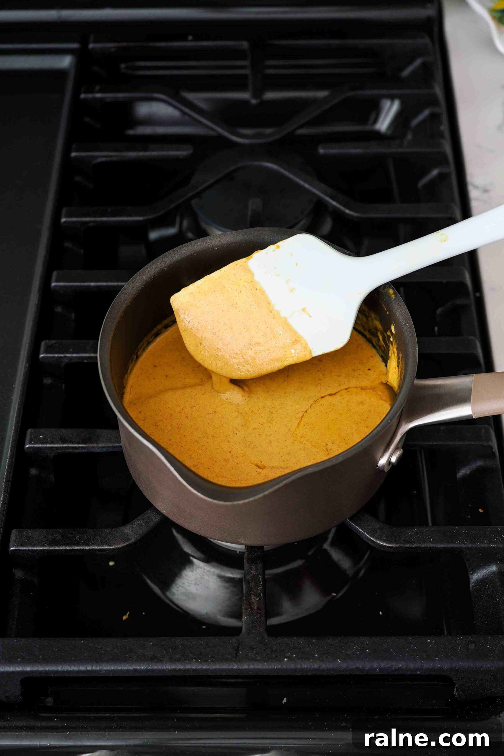 Pumpkin Spice Caramels Recipe: Homemade Fall Candy Guide 6 A spatula stirs together pumpkin cream over the stove.