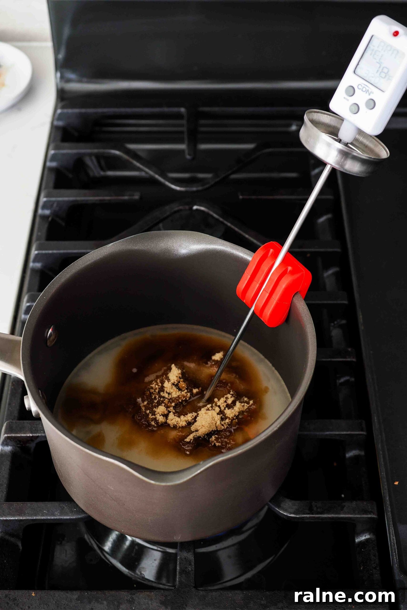Pumpkin Spice Caramels Recipe: Homemade Fall Candy Guide 7 Unmixed sugar, brown sugar, and corn syrup in a pot over the stove with a candy thermometer.