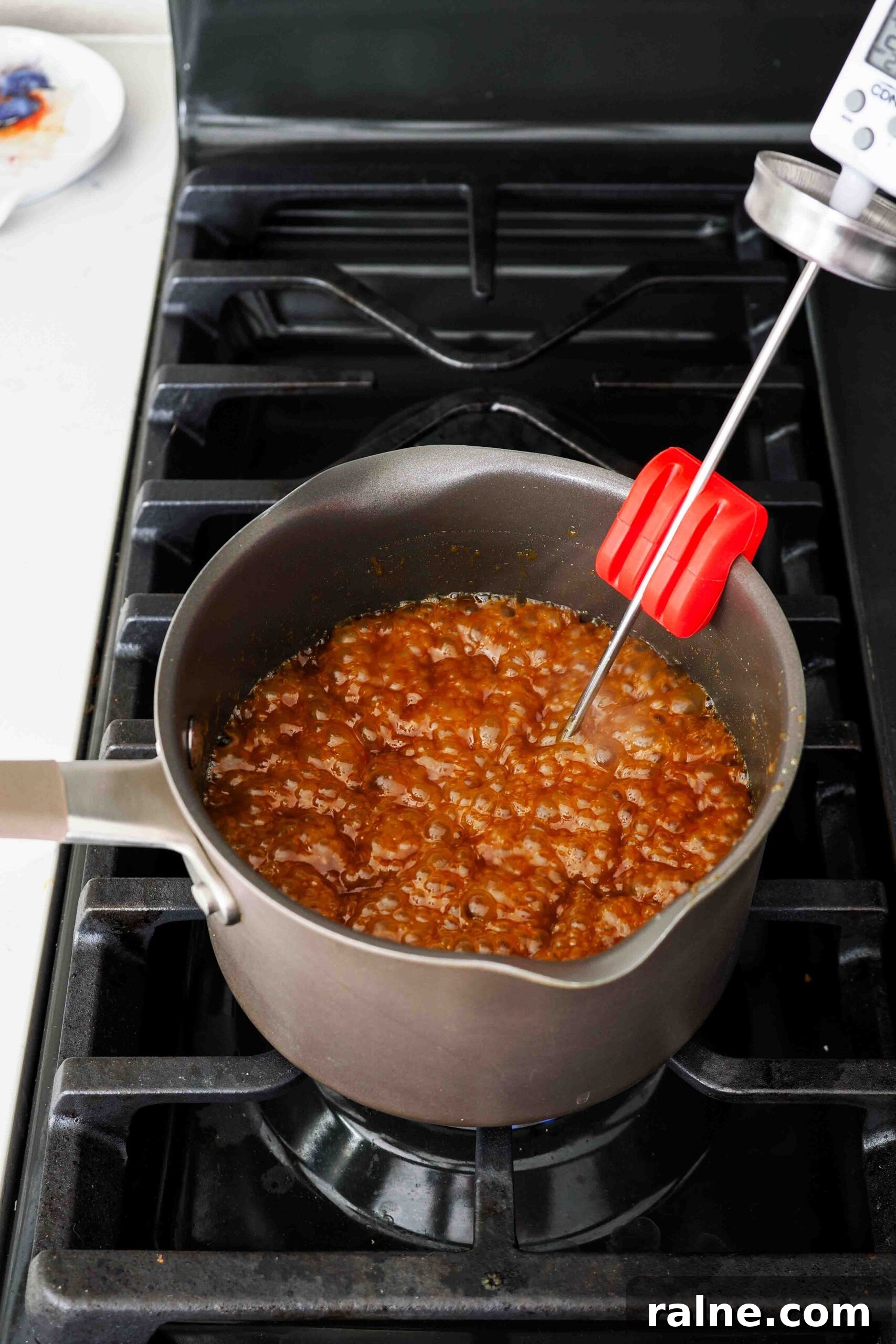 Pumpkin Spice Caramels Recipe: Homemade Fall Candy Guide 10 A pot of caramel over the stove with a candy thermometer.