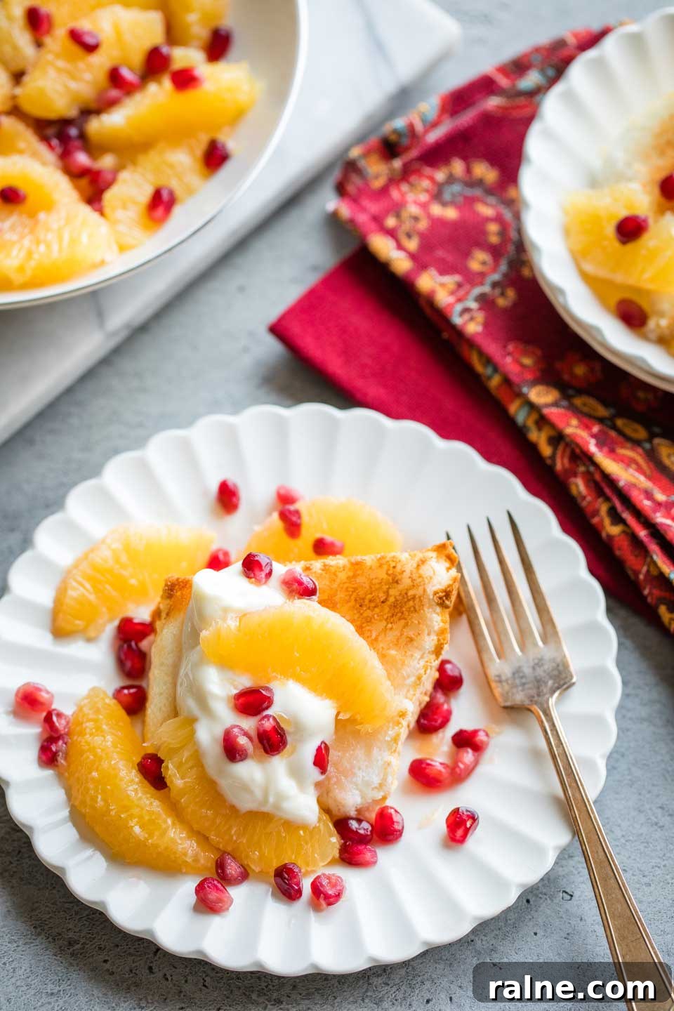 Healthy Angel Food Cake Dessert Recipe overhead of dessert on plate with a dollop of Greek yogurt and a gold fork, a second plated dessert and the bowl of remaining orange-pomegranate topping in the background