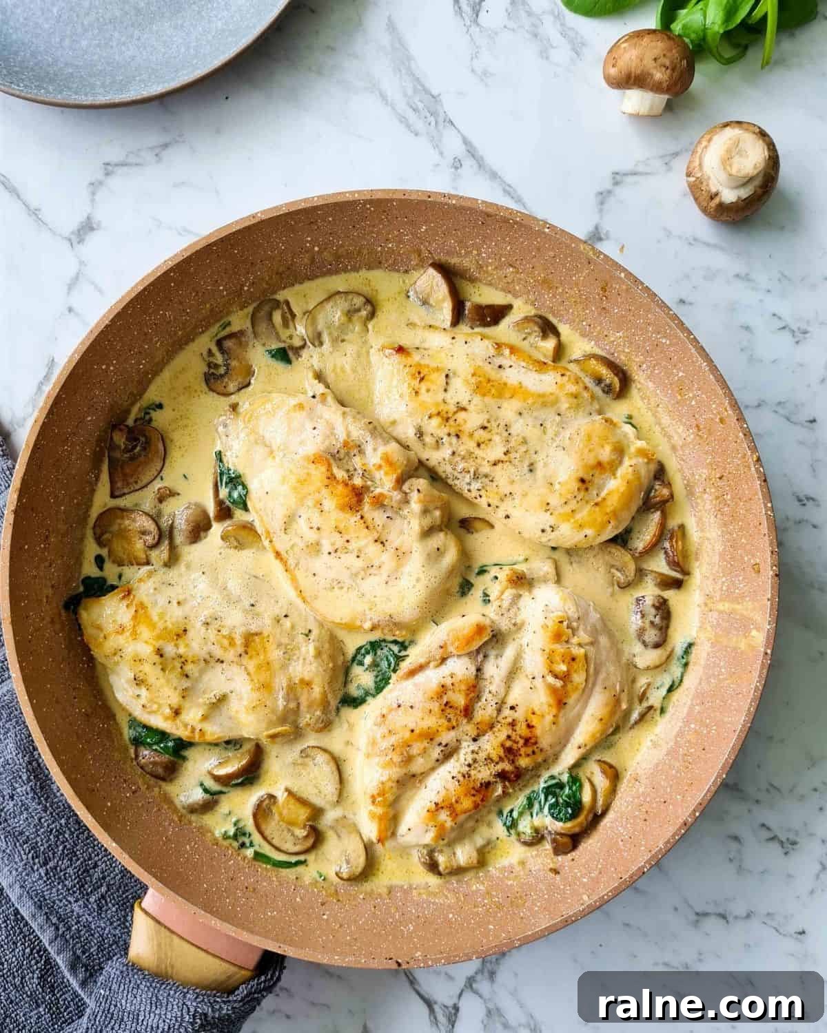 A pan of chicken breasts with creamy mushrooms and spinach straight off the stove