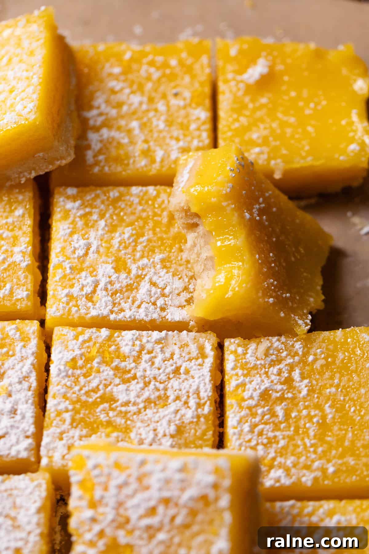 Classic Lemon Bars with Buttery Shortbread Crust 2 Lemon bars dusted with powdered sugar with one missing a bite.