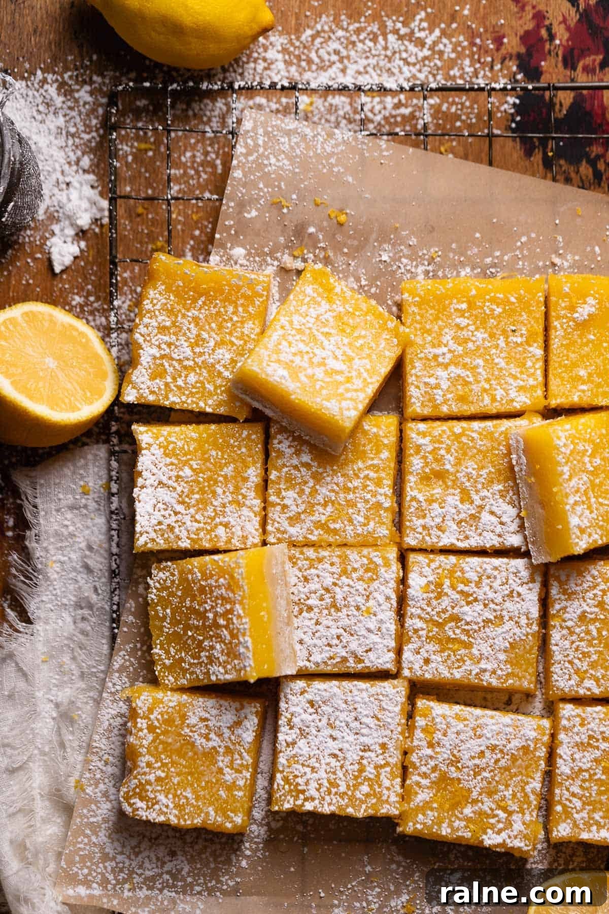 Classic Lemon Bars with Buttery Shortbread Crust 9 Lemon bars cut into squares and dusted with powdered sugar on brown parchment paper.