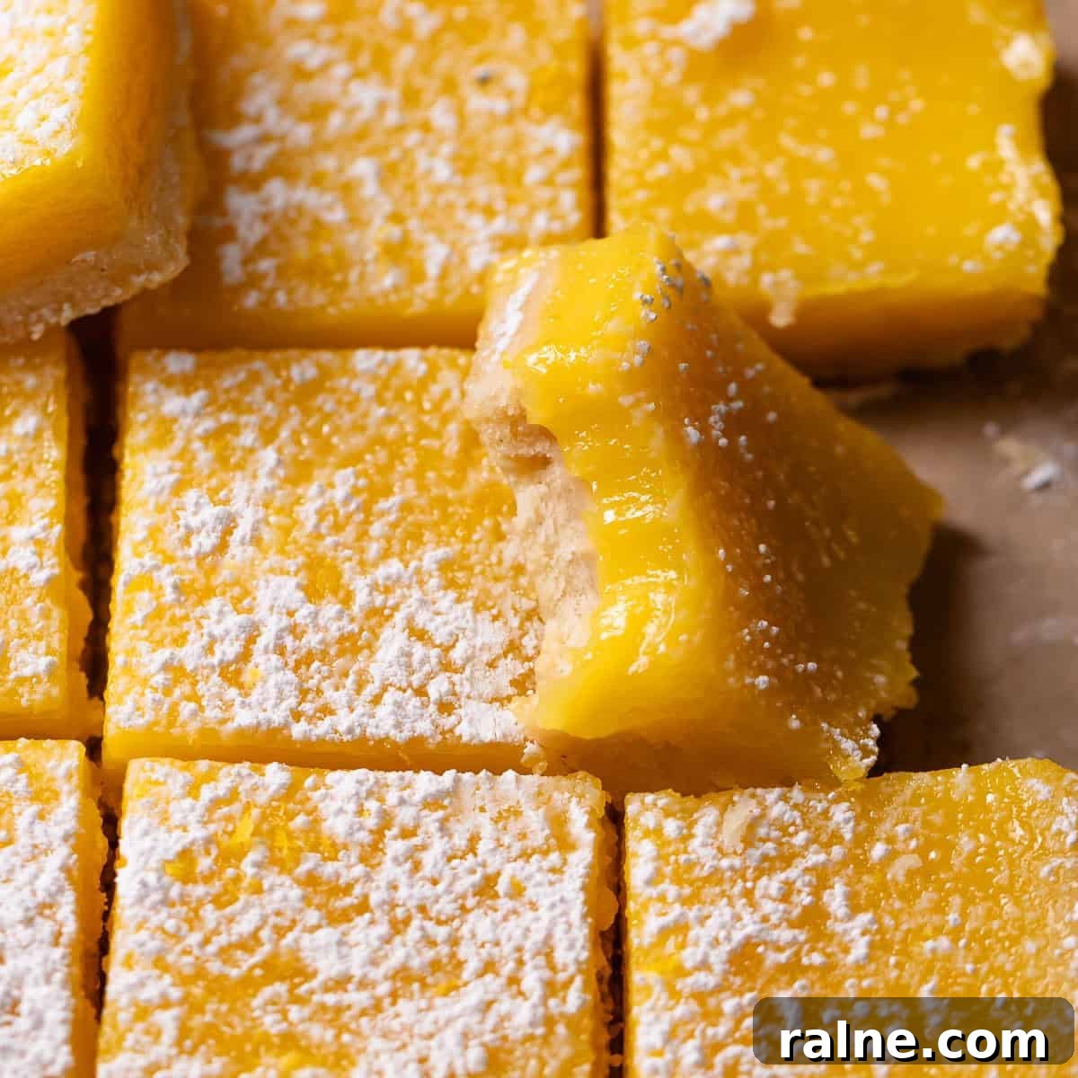 Classic Lemon Bars with Buttery Shortbread Crust 10 Lemon bars dusted with powdered sugar with one missing a bite.