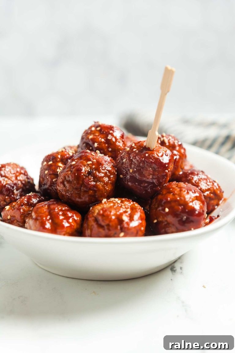 Spicy 4-Ingredient Cranberry Meatballs (Slow Cooker) 2 A white serving bowl filled with cranberry meatballs appetizers and a cocktail pick for serving them.