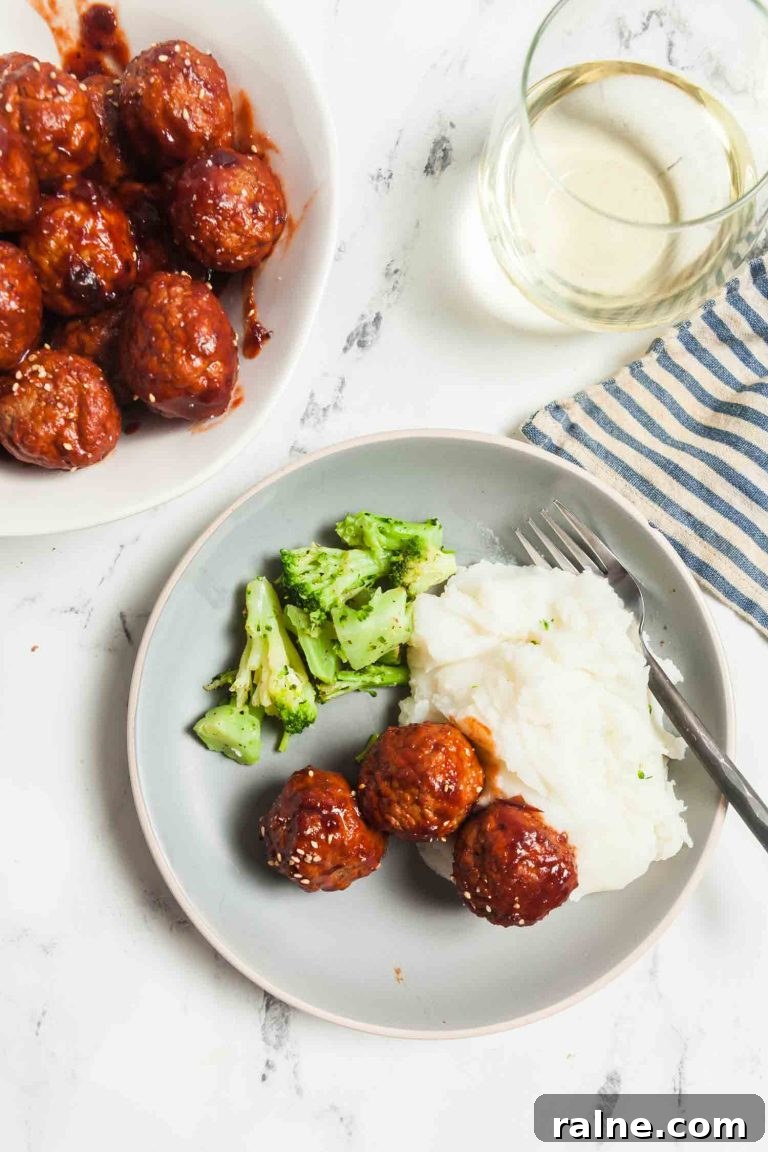 Spicy 4-Ingredient Cranberry Meatballs (Slow Cooker) 10 Overhead view of a light grey plate with cranberry glazed meatballs, mashed potatoes, and broccoli.